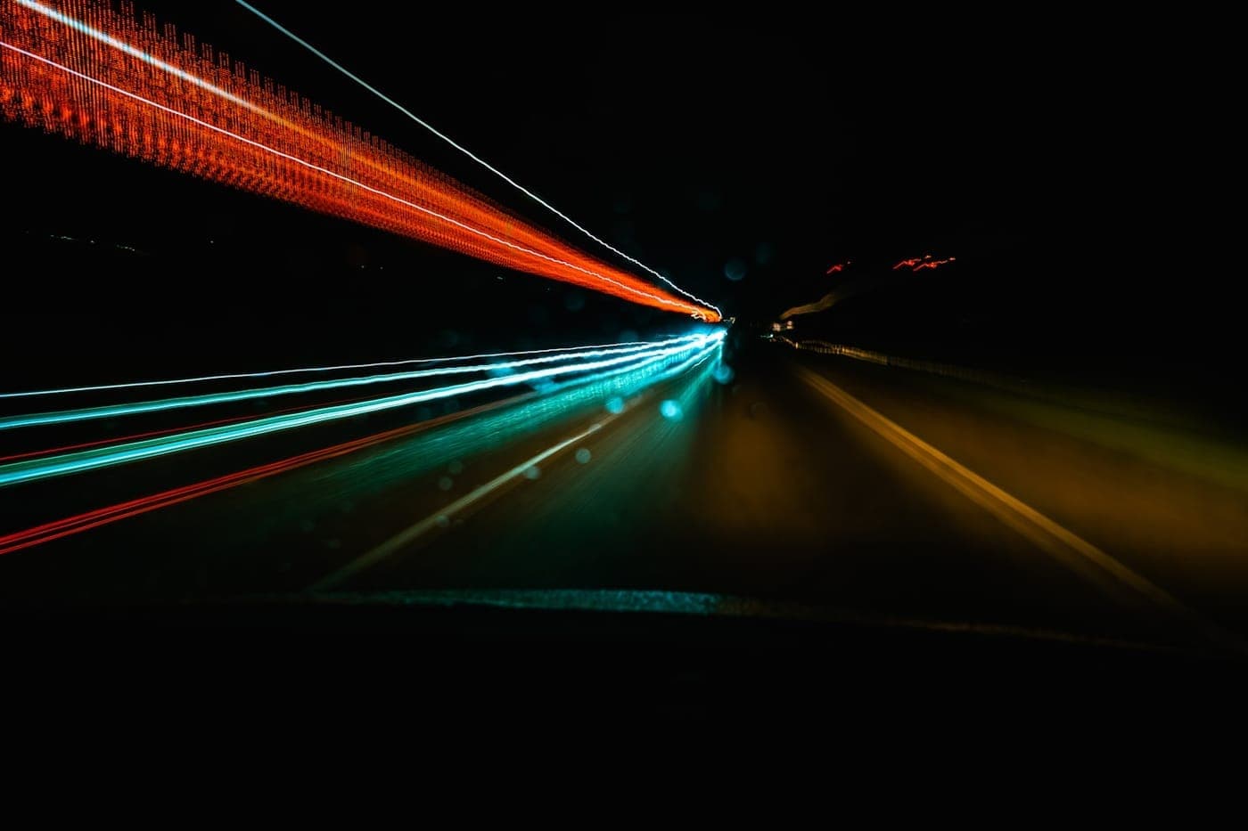 Long-exposure light trails of traffic streaking through the dark, evoking speed and motion
