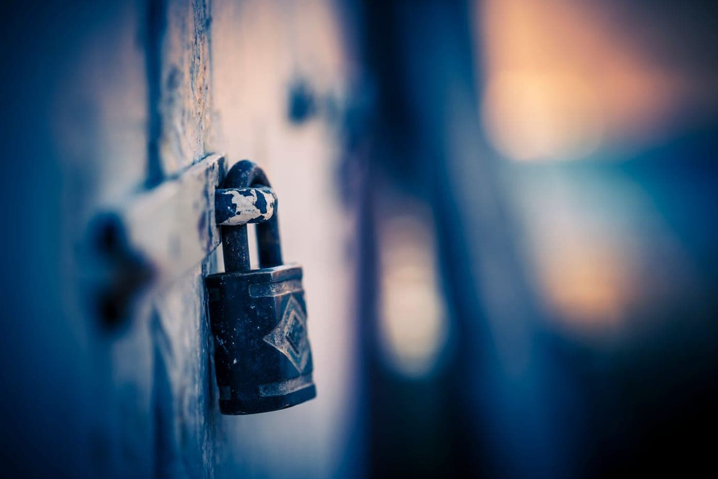 A weathered padlock locked onto a door against soft warm bokeh light